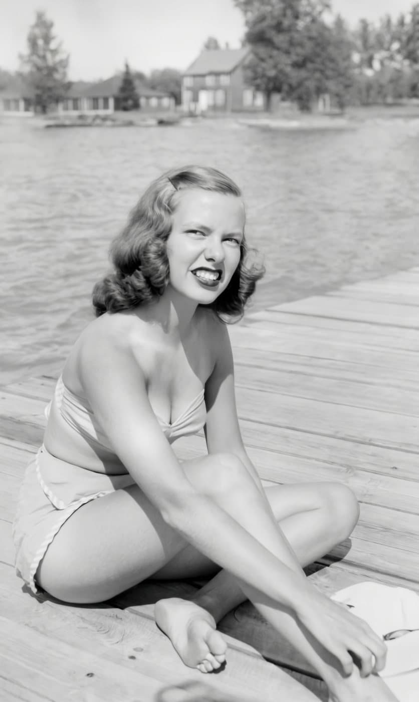 A 1945 black-and-white snapshot of a young woman on a lake dock, torn across the middle, restored